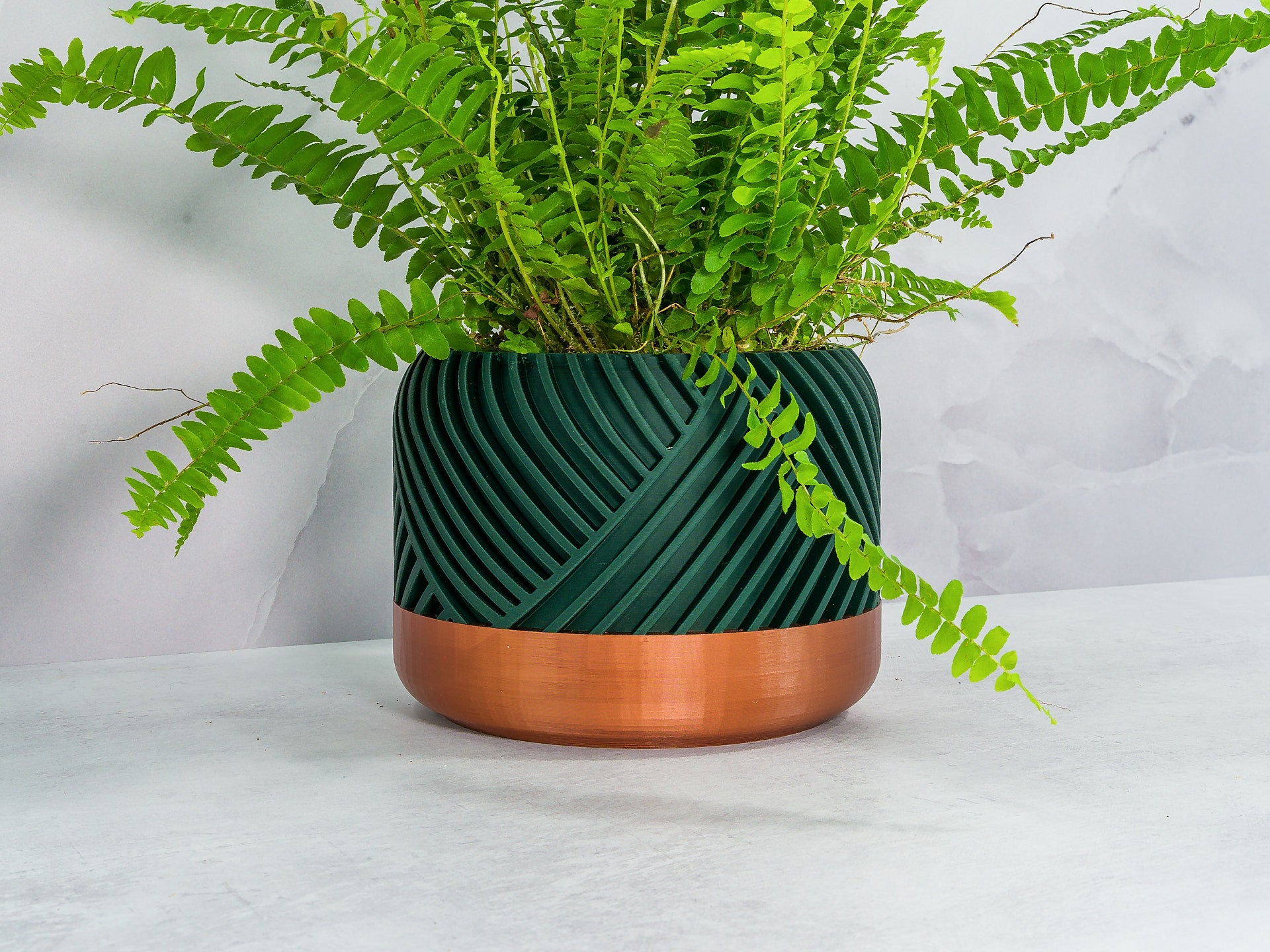 Angled with Fern: "Angled view of PEAK planter with copper base and forest pattern, showcasing a fern plant."
